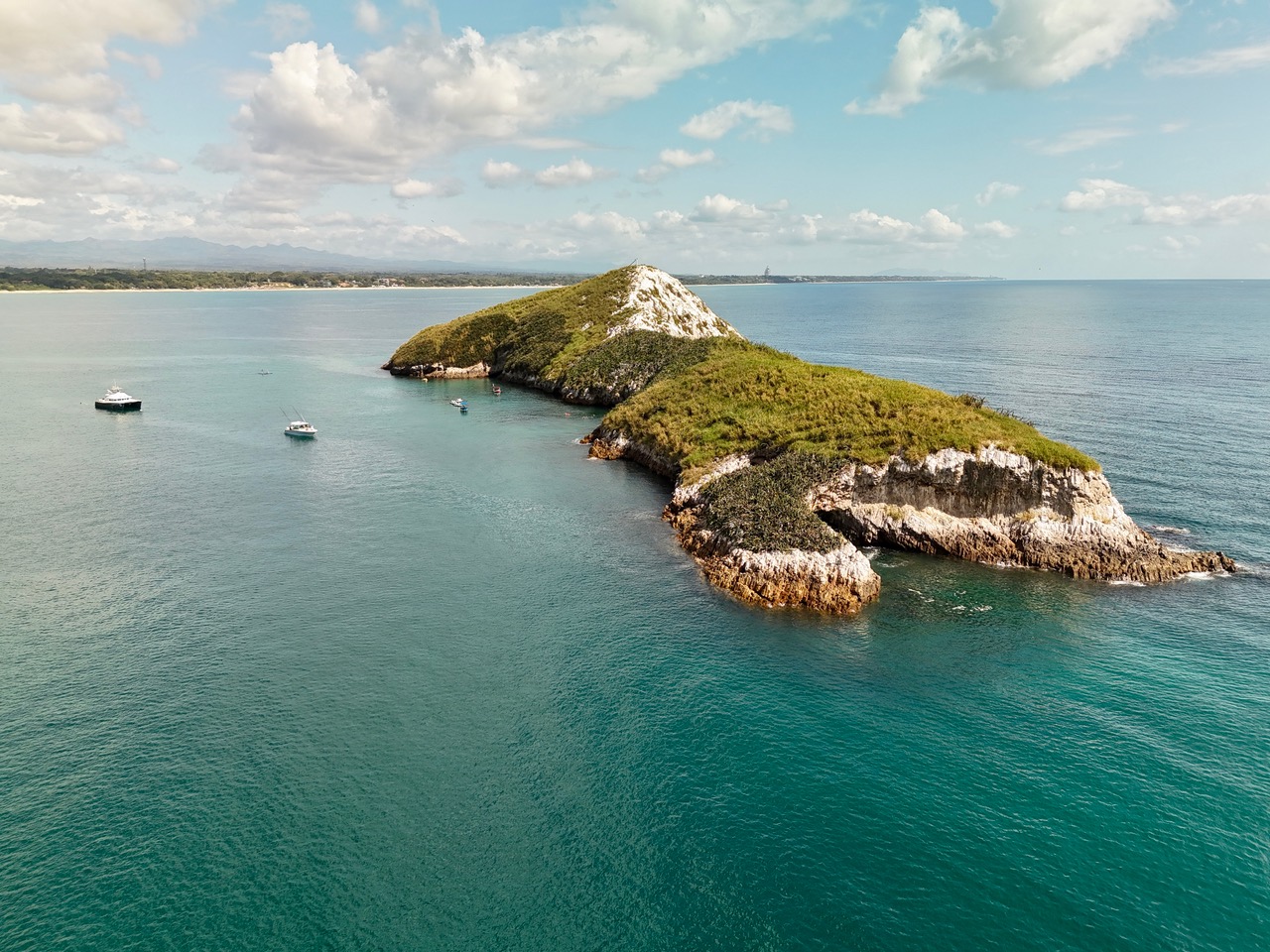 Isla Farallón from the water: two rocky headlands with green scrub on top and boats anchored in the bay between them