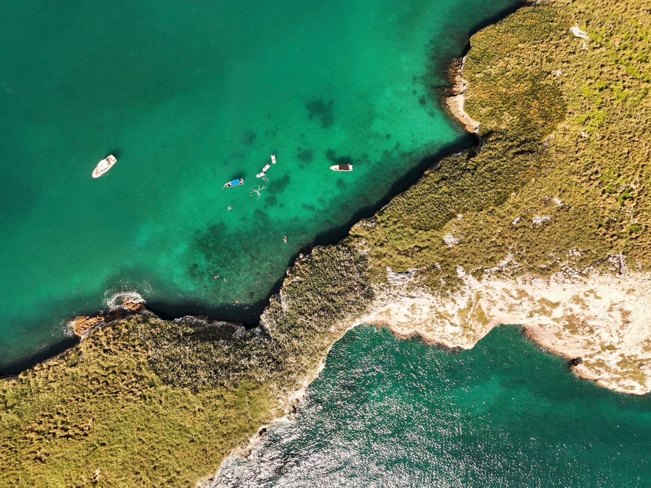 Looking straight down into the bay behind the island: boats at anchor and swimmers in clear green water
